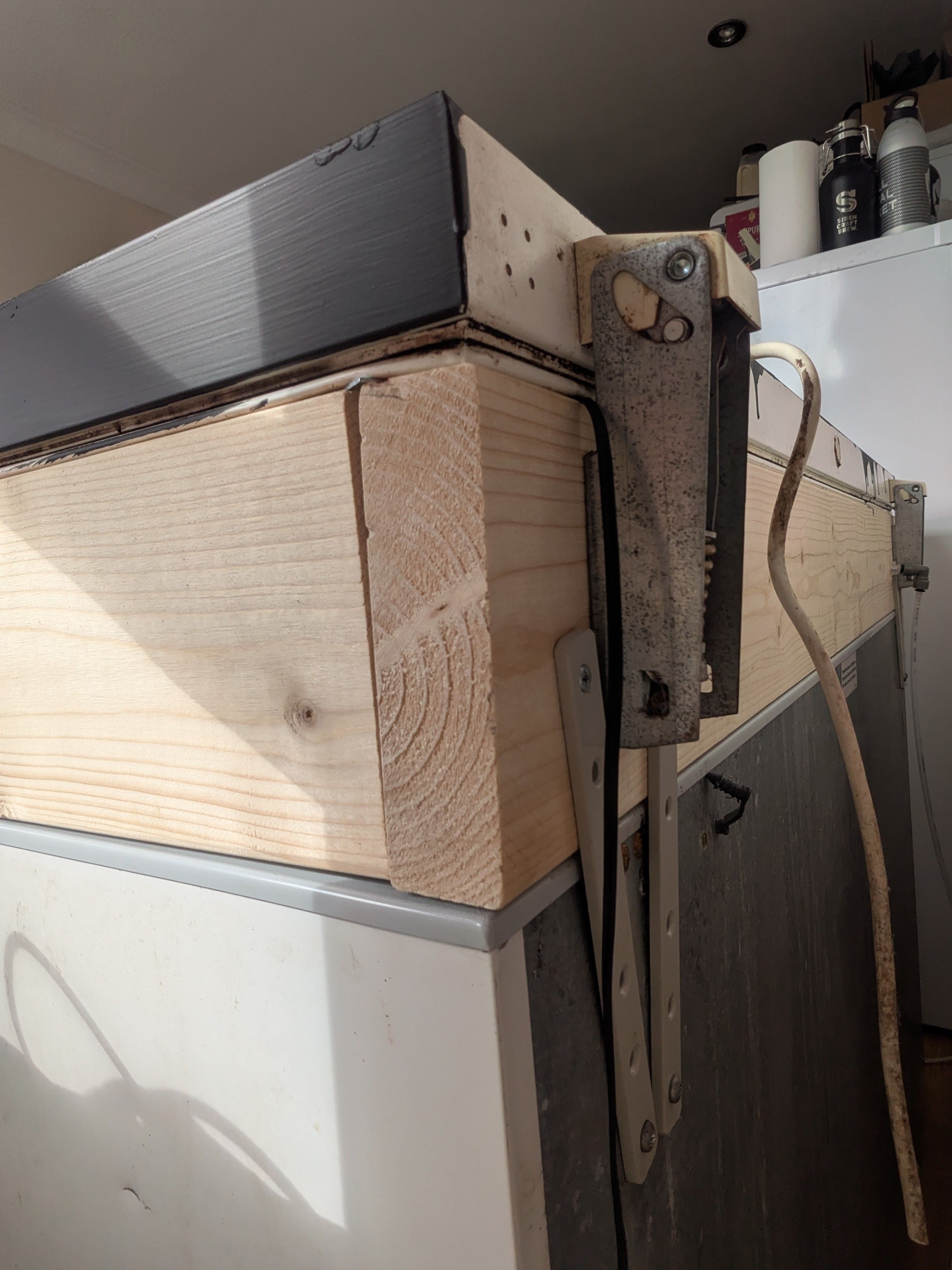 The lid hinge, screwed into the collar. Metal straps screwed into the body of both the freezer and the collar, to keep everything fastened together.